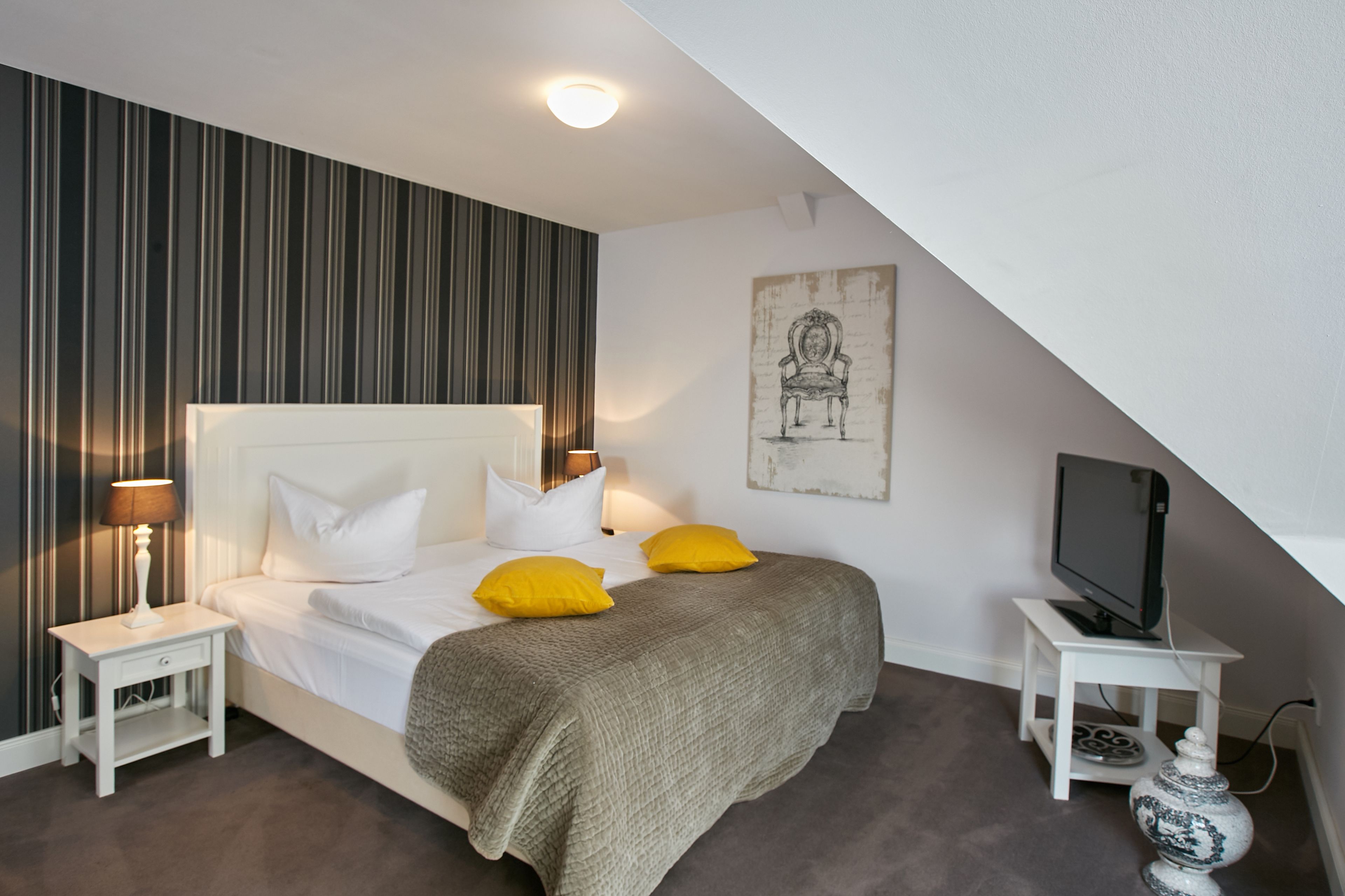 A bedroom with a bed, nightstands, a television, and a wall-mounted artwork.