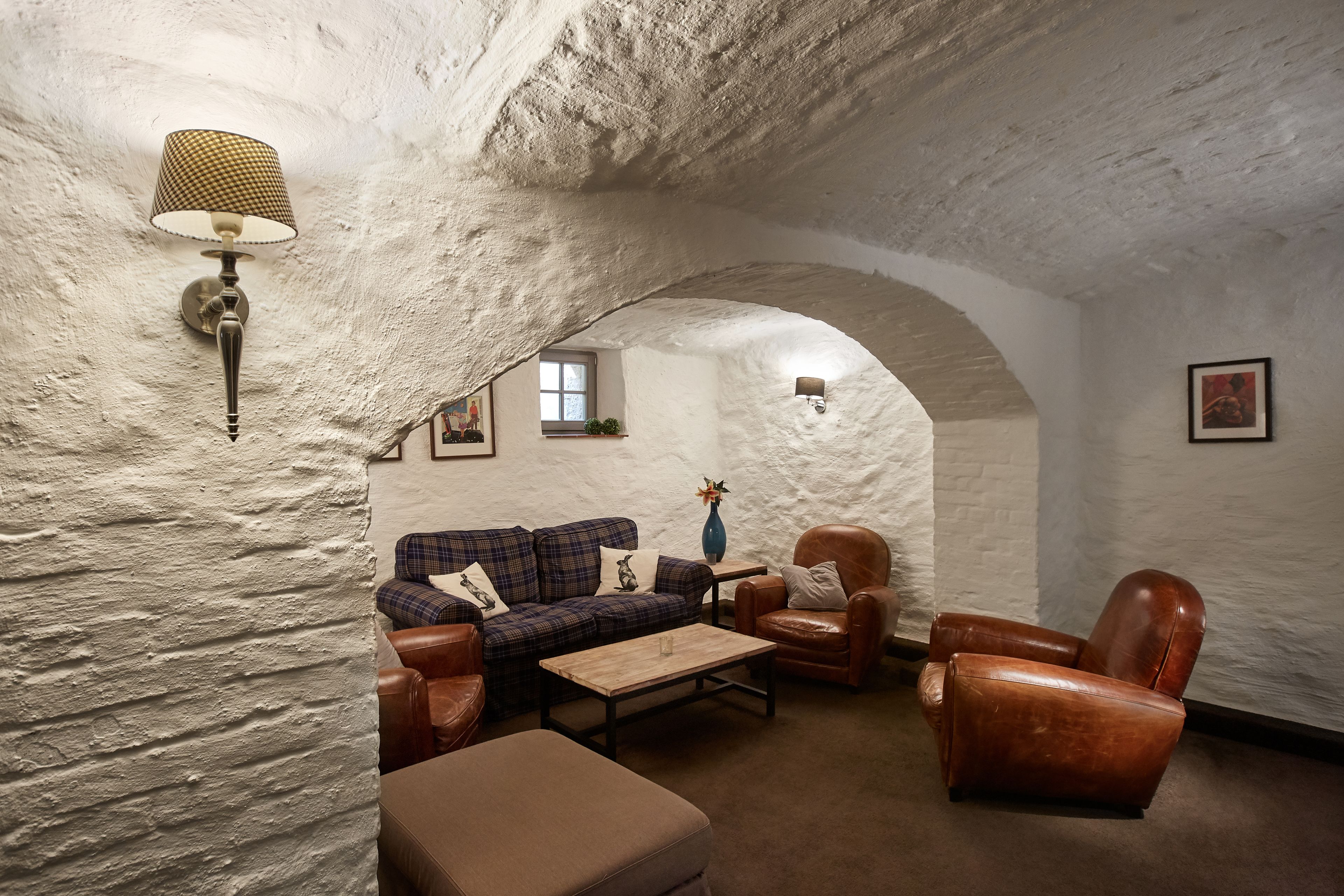 Een gezellige kamer met een geruit sofa, leren fauteuils, een houten salontafel en een lamp.