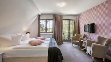 A hotel room with a bed, two armchairs, a small table, and a TV mounted on the wall.
