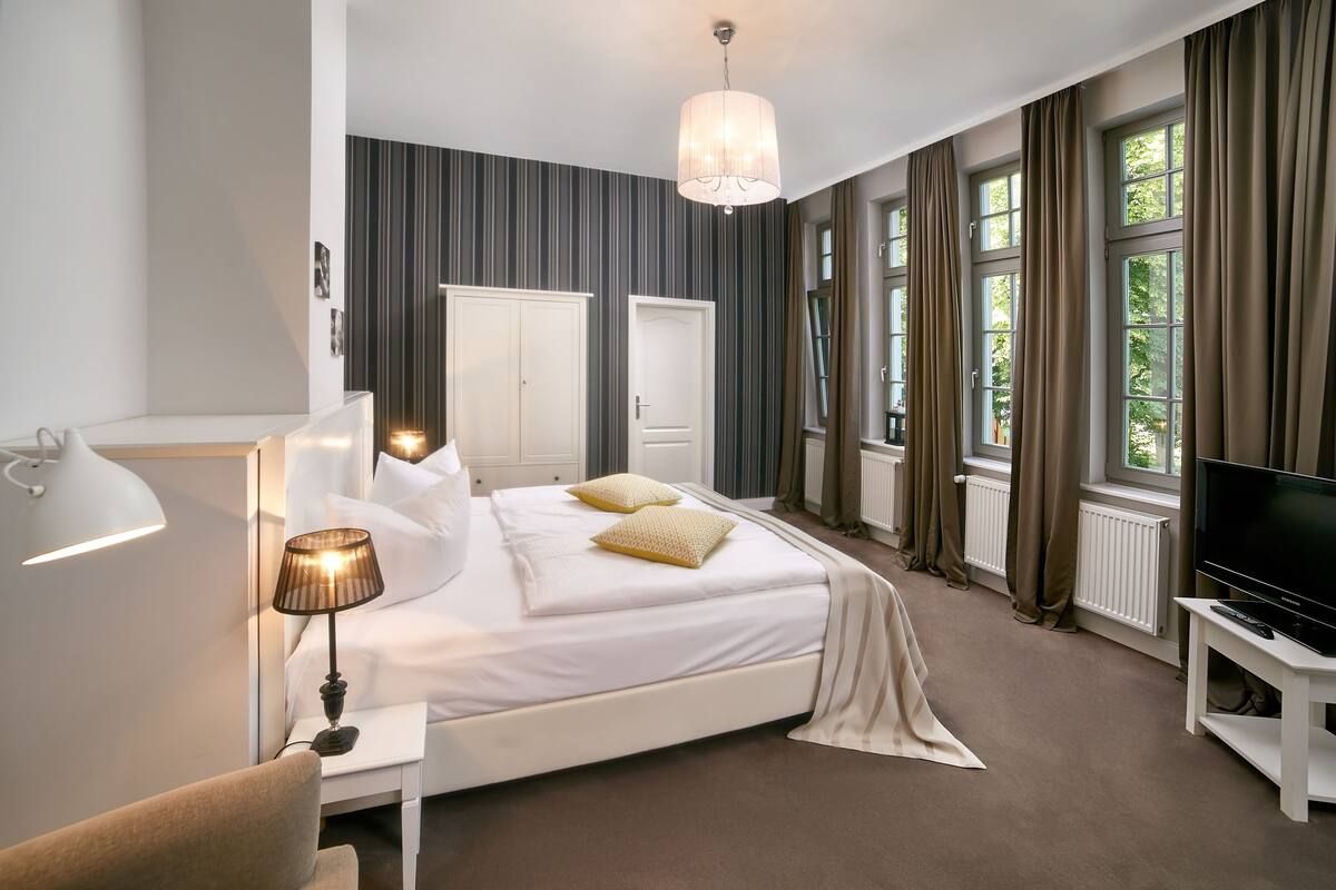 A modern hotel room with a large bed, a TV, a desk, and a lamp.