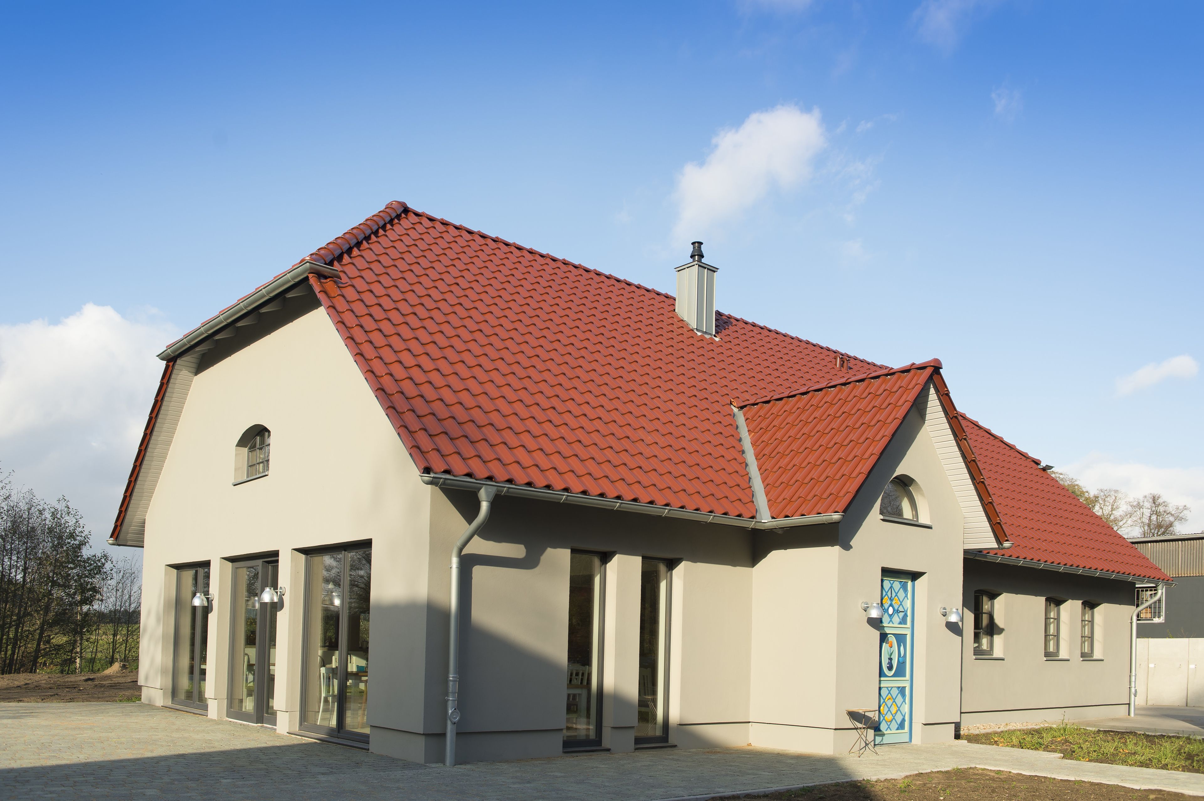 Ein modernes Gebäude mit roten Ziegeldach, großen Fenstern und einer blauen Tür.