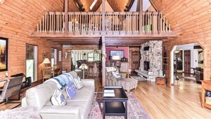 A spacious loft-style living area with a high ceiling, wooden beams, and a balcony. - Gorgeous large lakefront home with firepit and a private dock! (ST GERMAIN)