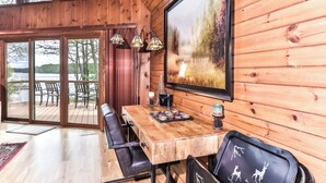 A wooden interior with a dining table, chairs, and a large window overlooking a lake. - Gorgeous large lakefront home with firepit and a private dock! (ST GERMAIN)