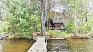 A wooden dock leading to a cabin surrounded by trees. - Gorgeous large lakefront home with firepit and a private dock! (ST GERMAIN)