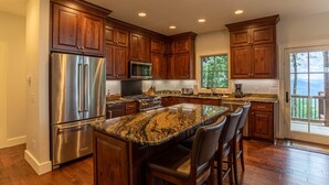 A modern kitchen with wooden cabinets, stainless steel appliances, and a granite island with bar stools.
