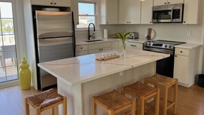 A modern kitchen with white cabinetry, stainless steel appliances, a large island with bar stools, and pendant lighting. - Open Floor Plan, Family Friendly, Waterview Home  (Narragansett)