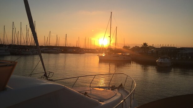 Ein Yachthafen mit mehreren vertäuten Booten, ein klarer Himmel und ein Sonnenuntergang im Hintergrund.