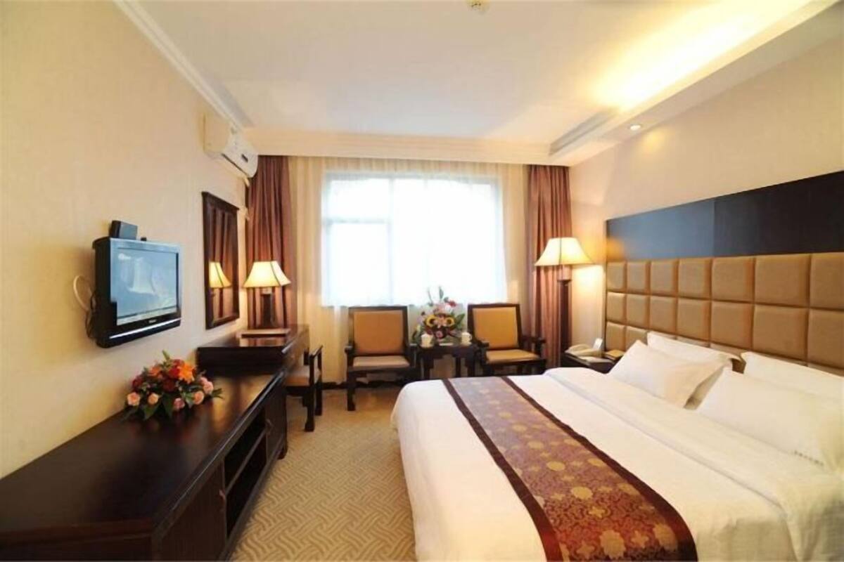 Habitación de hotel con cama, escritorio con televisor, dos sillones, lámpara de escritorio, teléfono y ventana con cortinas.
