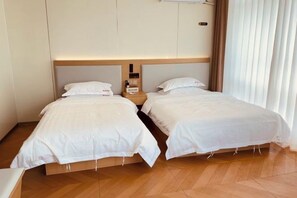 Una habitación de hotel con dos camas individuales, un cabecero de madera, una mesita de noche y una ventana con cortinas.