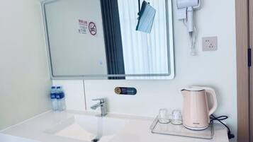 A hotel bathroom with a sink, mirror, towel dispenser, and a kettle on the counter.