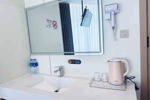 A hotel bathroom with a sink, mirror, towel dispenser, and a kettle on the counter. - Shanghai Xinjiangnan Hotel (Shanghai)