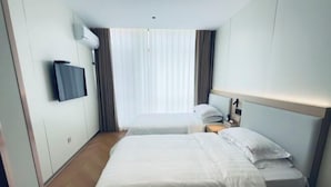 Et hotelværelse med seng, fjernsyn, et vindue med gardiner og en sengegavl.