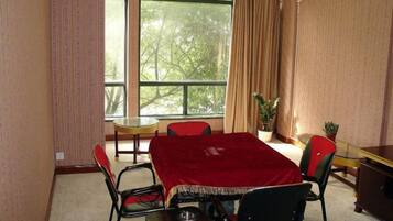 A dining area with a table covered by a red tablecloth, surrounded by chairs, and a window with curtains.