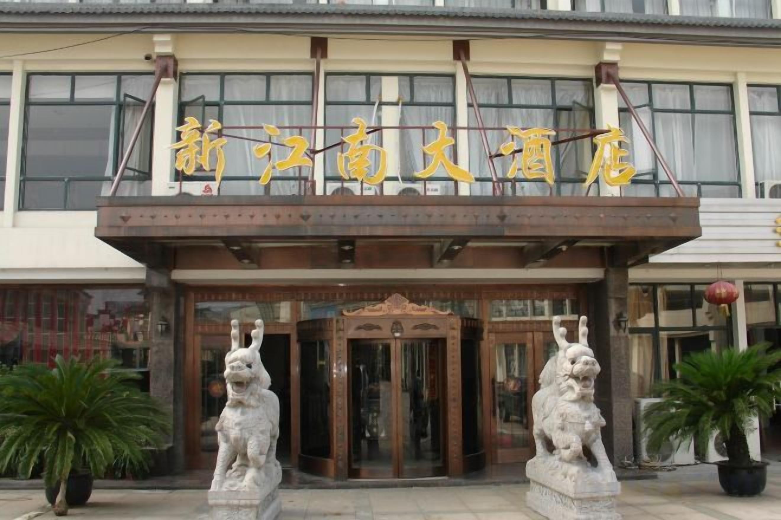 A hotel entrance with a traditional Chinese architectural style, featuring a wooden facade and two stone lion statues at the entrance.