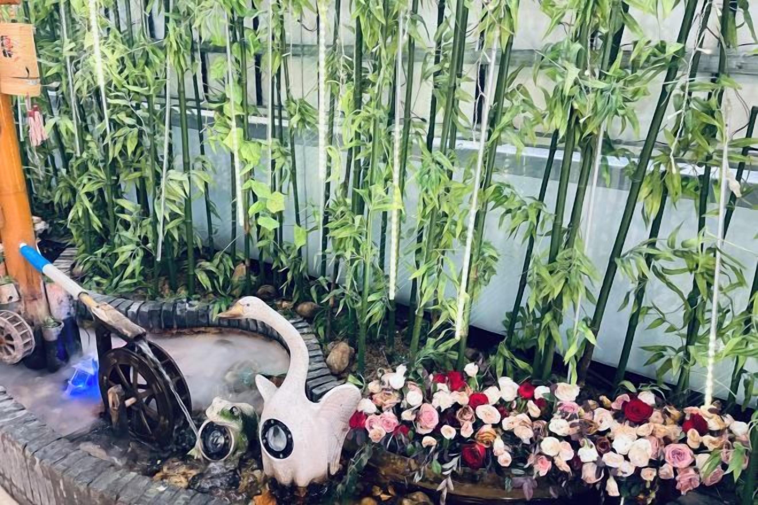 Un jardín decorativo con una escultura de cisne, plantas de bambú y un arreglo floral.