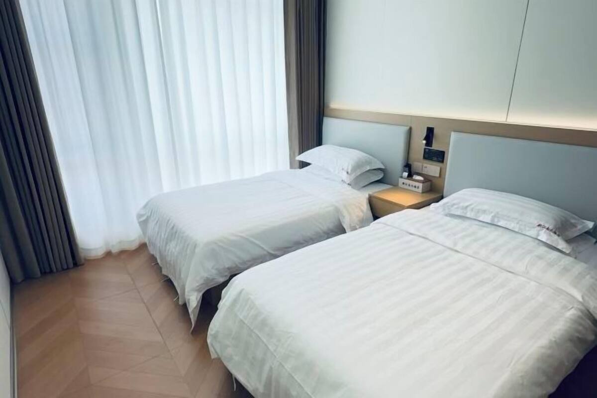 Habitación de hotel con dos camas, una mesita de noche y un ventanal con cortinas.