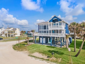A two-story beachfront house with a balcony, a covered porch, and a view of the ocean.
