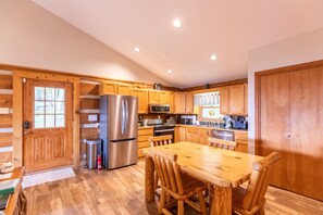 A kitchen with wooden cabinets, stainless steel appliances, and a wooden dining table.