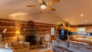 A cozy cabin interior with a stone fireplace, wooden furniture, and a kitchen area. - Silverleaf - 30 Mile View, Hot Tub, Close to ASU (Zionville)