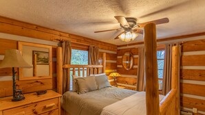 A wooden cabin bedroom with a four-poster bed, wooden nightstands, a ceiling fan, and a window with curtains. - Silverleaf - 30 Mile View, Hot Tub, Close to ASU (Zionville)