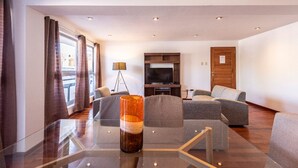 Habitación de hotel moderna con una mesa de vidrio, un conjunto de sofá, televisor de pantalla plana y vistas al exterior a través de amplias ventanas.