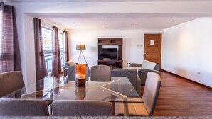 Una sala de estar moderna con una mesa de comedor de vidrio, sofás grises, un televisor de pantalla plana y un mueble de madera.
