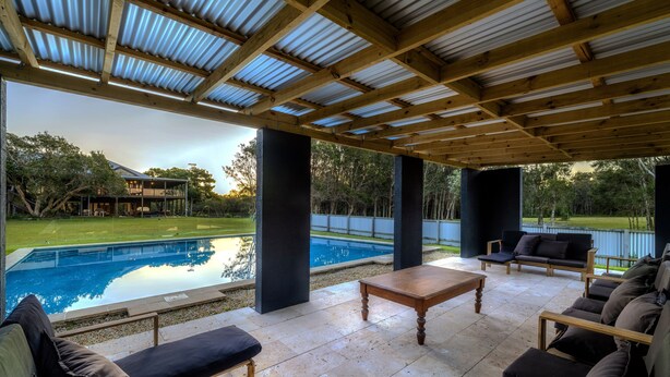 A covered outdoor patio with a pool, seating area, and a view of a house in the background. - Tranquilo Beach House (Woolgoolga)