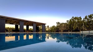 Une piscine dotée d’un espace couvert et de chaises longues, entourée d’arbres.