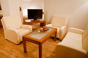A living room with two beige sofas, a wooden coffee table with fruit, and a TV on a stand. - Hotel Vabank (Golub-Dobrzyń)
