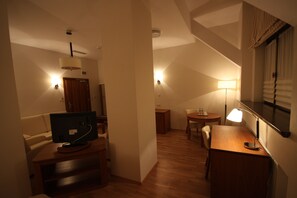 A cozy room with a wooden desk, a television, a lamp, and a small dining table. - Hotel Vabank (Golub-Dobrzyń)
