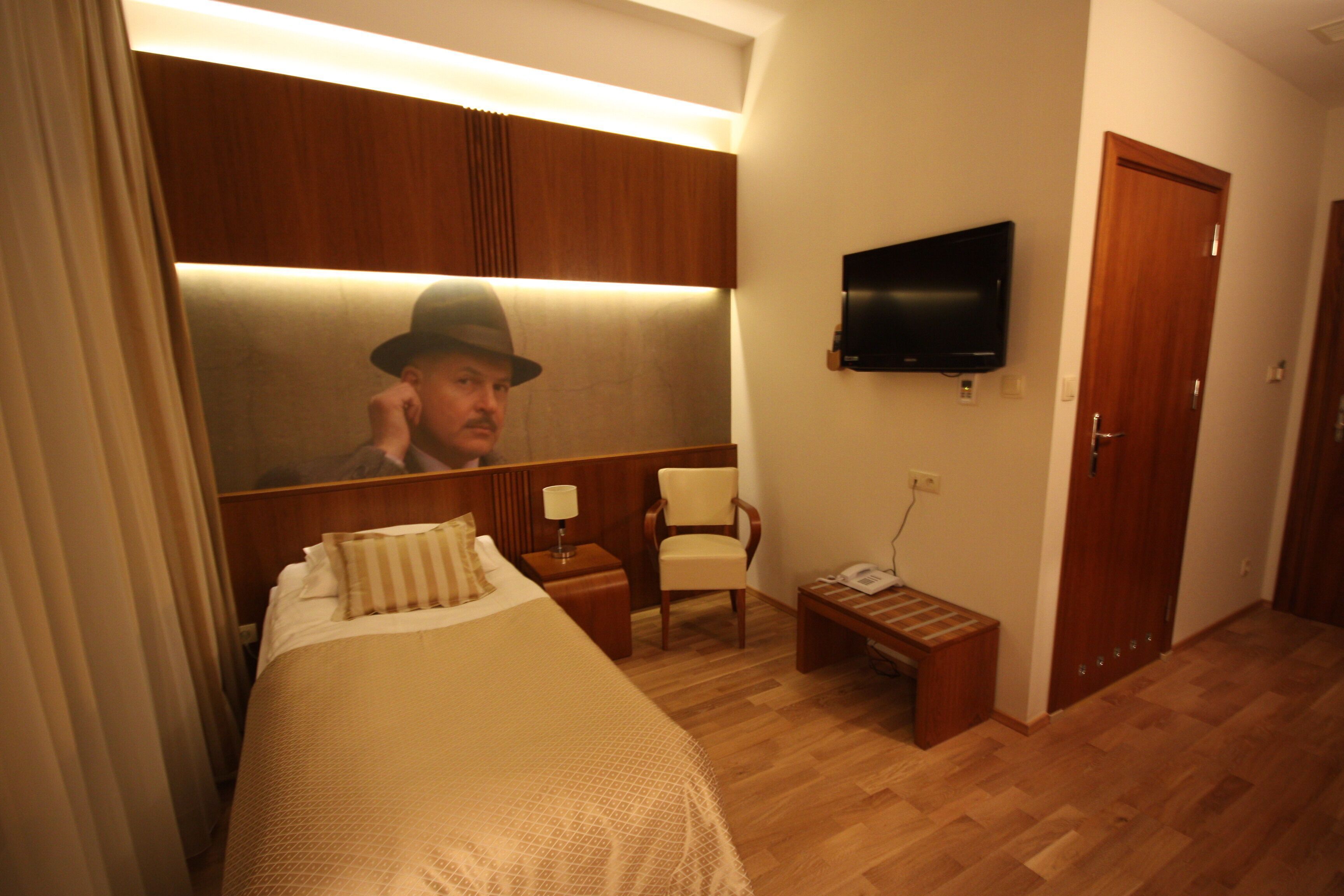 A hotel room with a bed, a chair, a bedside table, a television, and a wooden wardrobe.