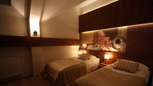 Quarto de hotel com duas camas de solteiro, uma cabeceira de madeira, um quadro pendurado na parede e um abajur.