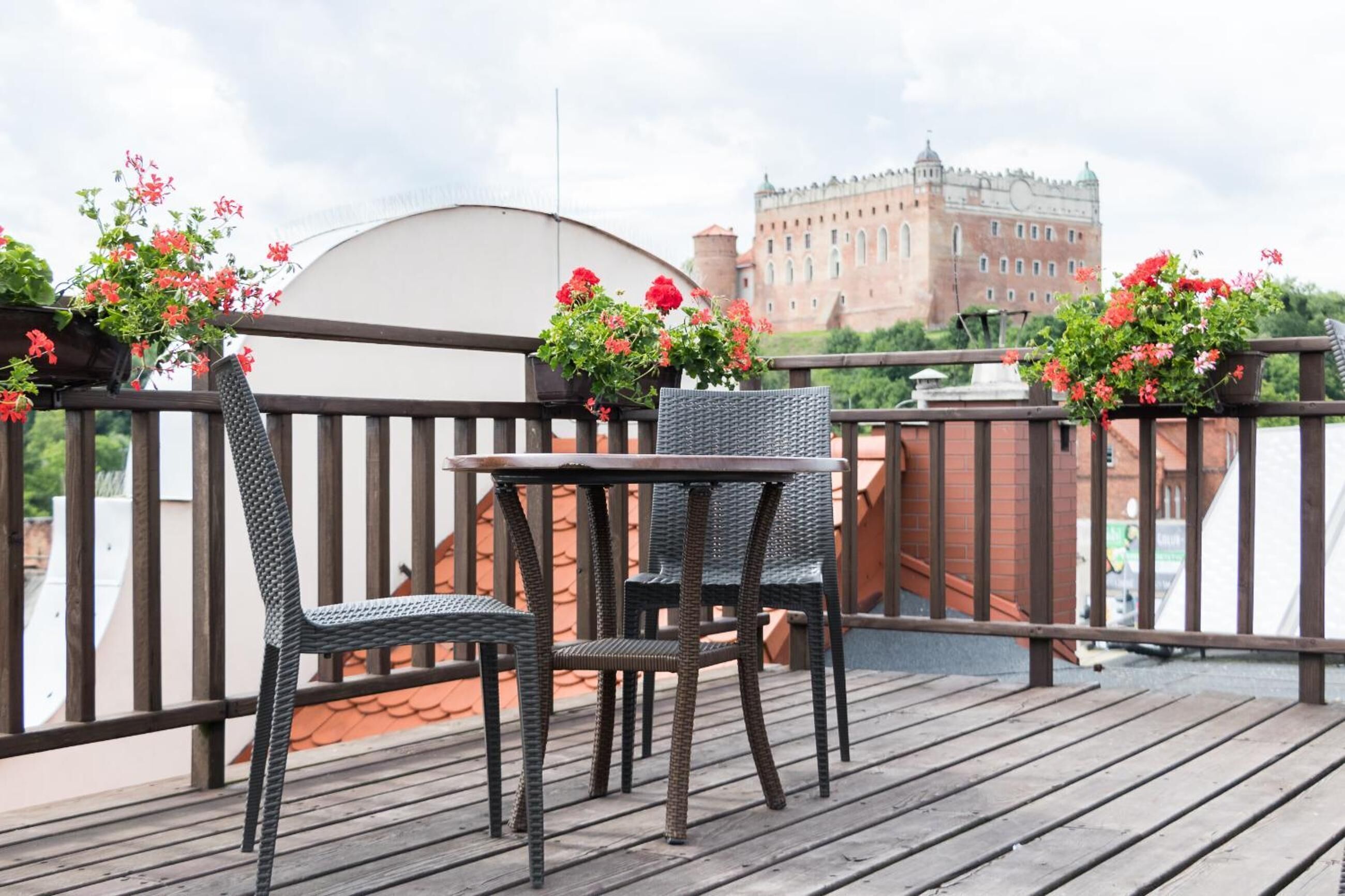Eine Holzdielen-Terrasse mit Korbstühlen und einem Tisch, mit Blick auf eine Burg.