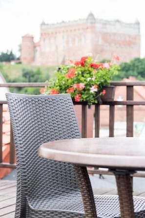 A wicker chair and table on an outdoor deck with a view of a building in the background. - Hotel Vabank (Golub-Dobrzyń)