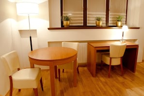A dining area with a wooden table, two chairs, a radiator, and a window with blinds. - Hotel Vabank (Golub-Dobrzyń)