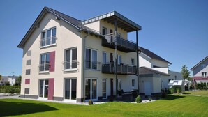 Un immeuble résidentiel à plusieurs étages, doté de balcons, de grandes fenêtres et d’une pelouse bien entretenue.