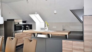 Une cuisine moderne dotée d’un îlot central, d’appareils électroménagers intégrés et de luminaires suspendus.