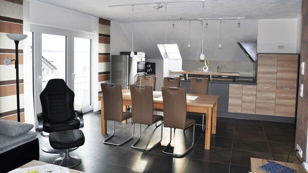 Une cuisine moderne avec un coin repas, comprenant une table avec des chaises, un tabouret de bar et une vue sur l’extérieur.