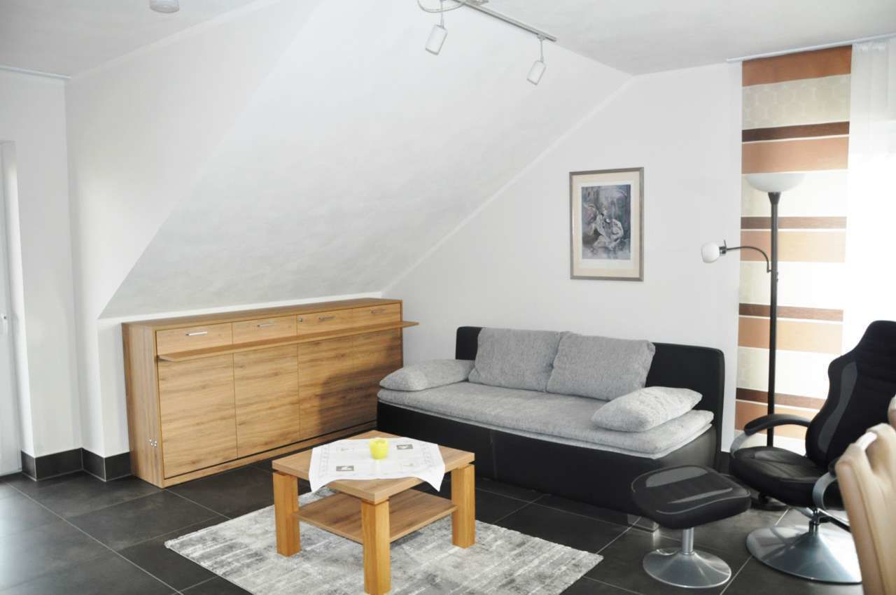 Un salon moderne avec un meuble en bois, un canapé gris, un fauteuil noir et une petite table en bois sur laquelle repose un livre.