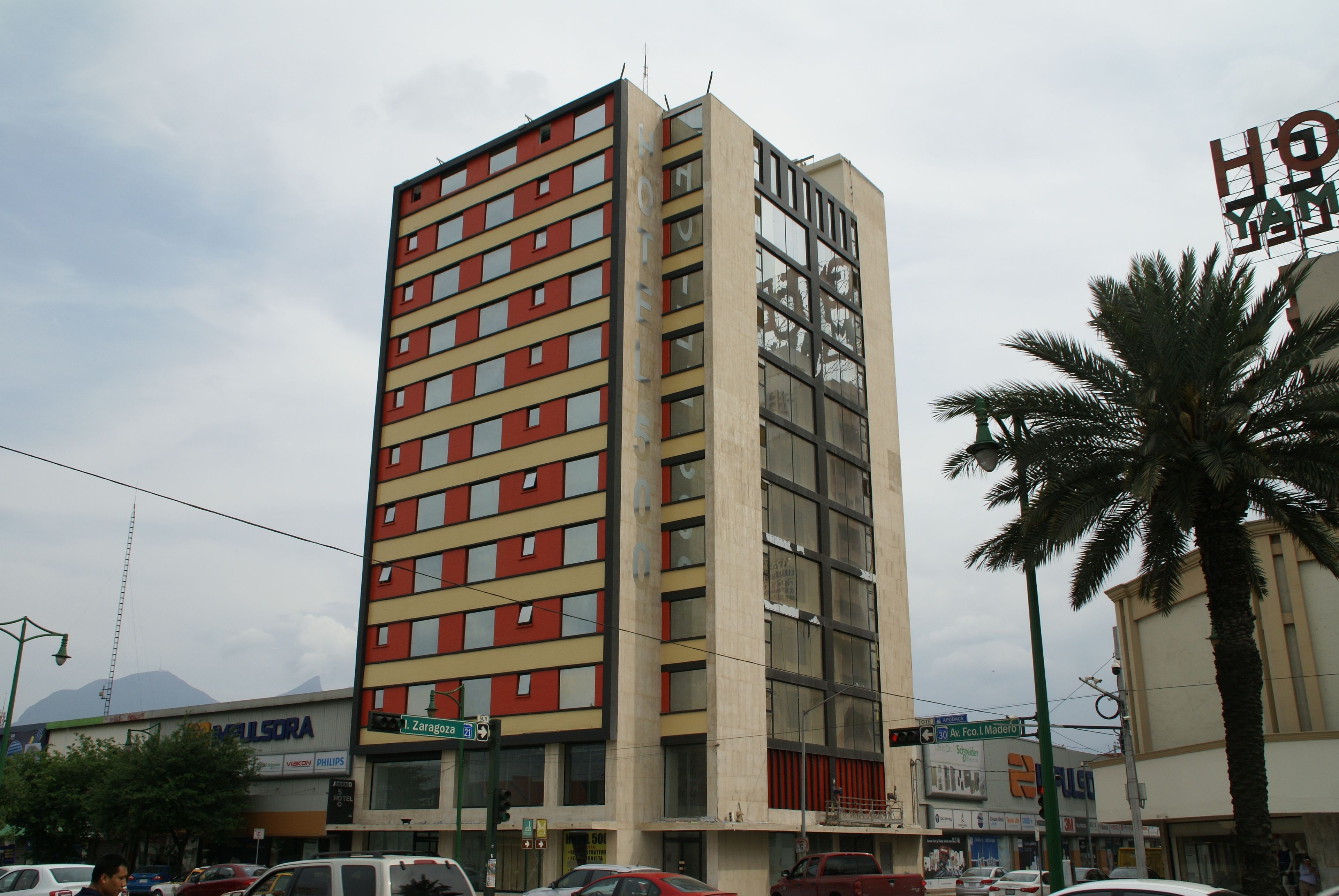 Un grand hôtel à plusieurs étages, doté de grandes fenêtres et d’une enseigne bien visible indiquant « Hôtel Yama ».