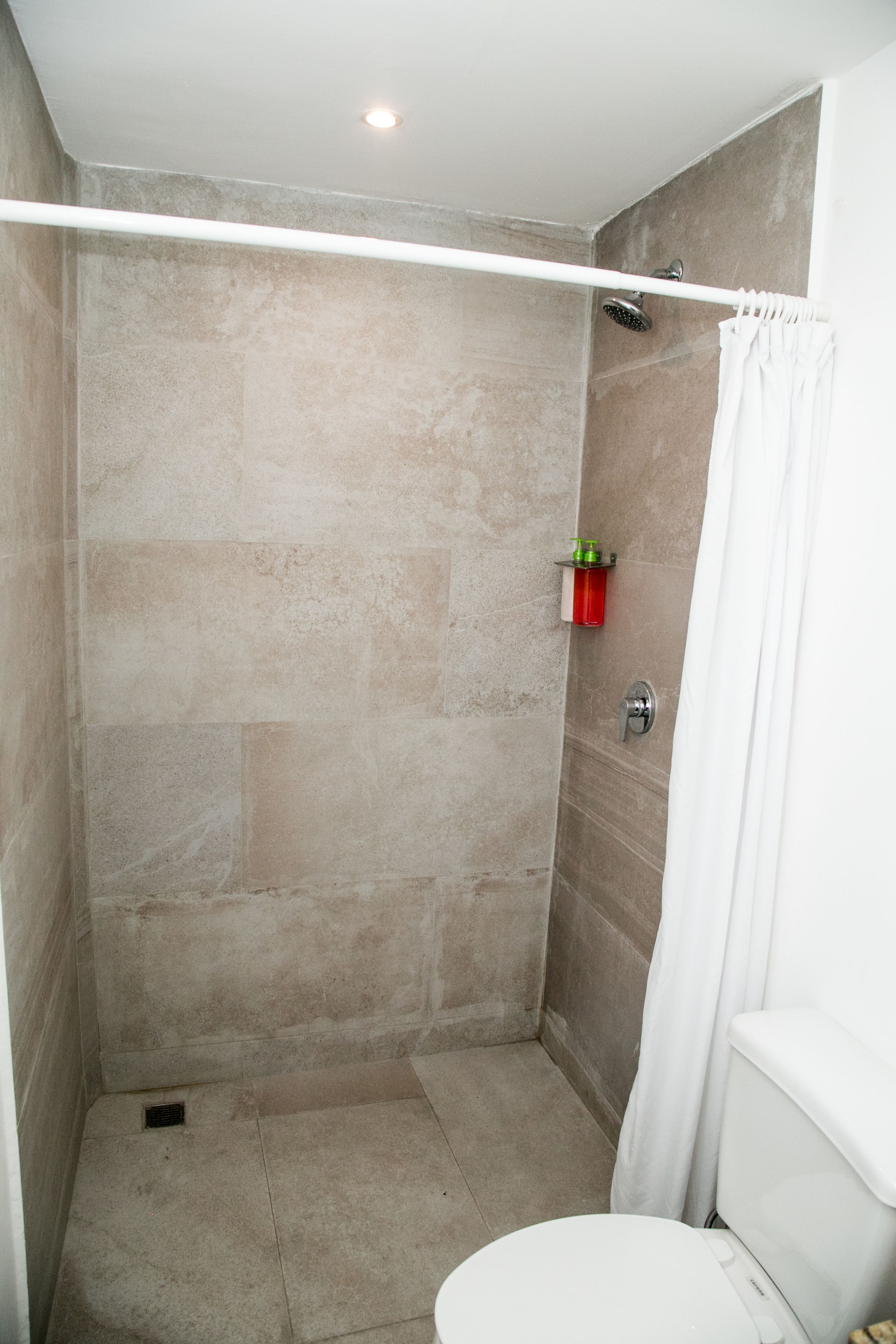 A shower area with a glass door, a white toilet, and a small shelf with toiletries.