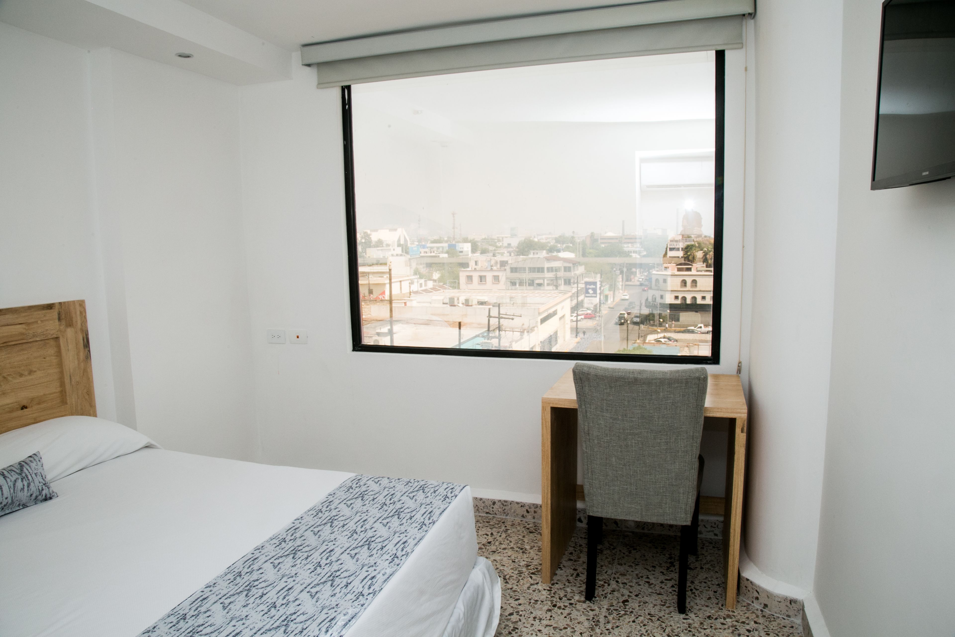 A hotel room with a bed, a desk, and a large window offering a city view.