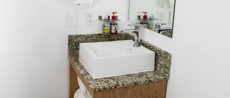 Un baño con lavamanos blanco, tocador de madera y un inodoro.