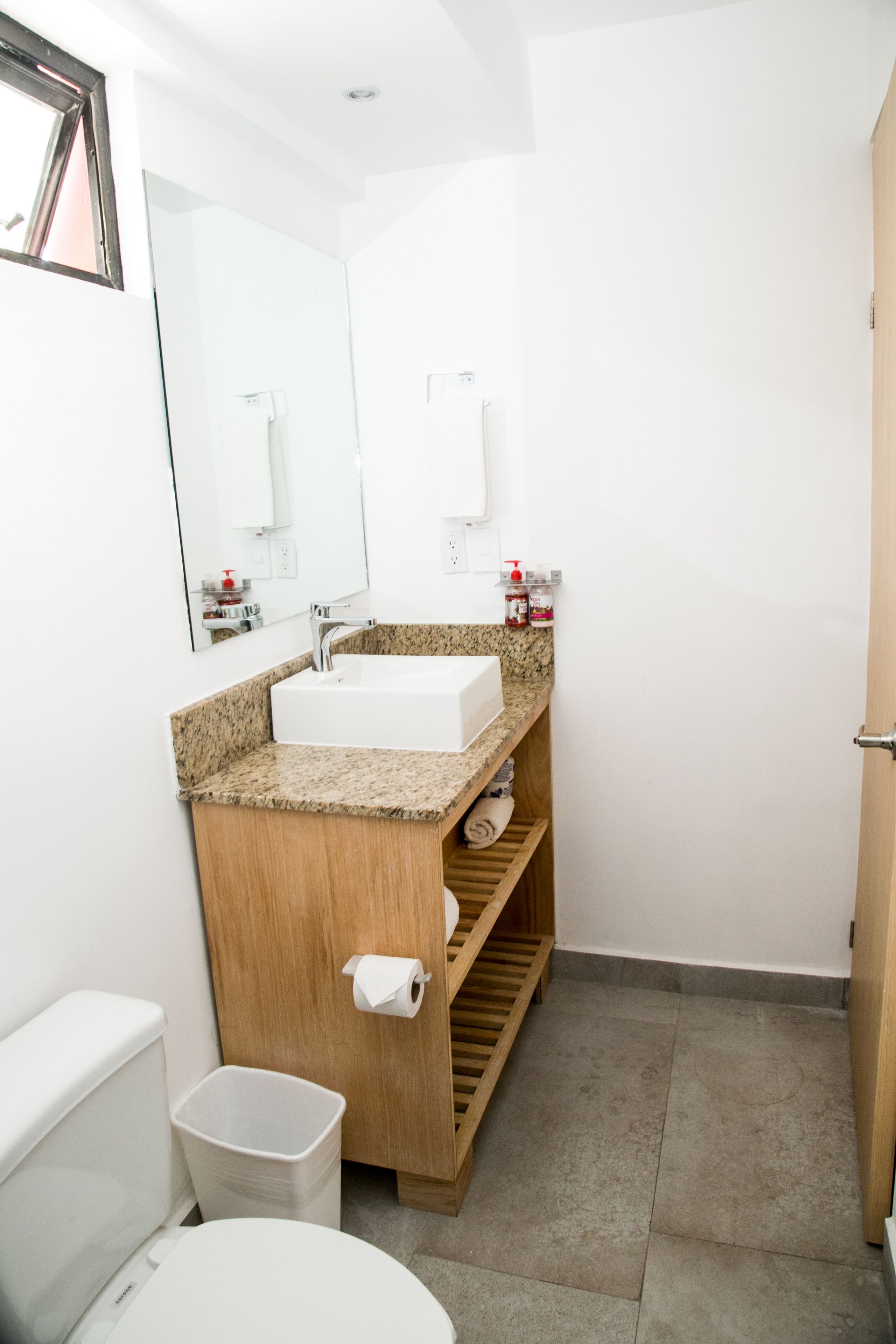 A modern bathroom with a white sink, granite countertop, wooden vanity, and a large mirror.