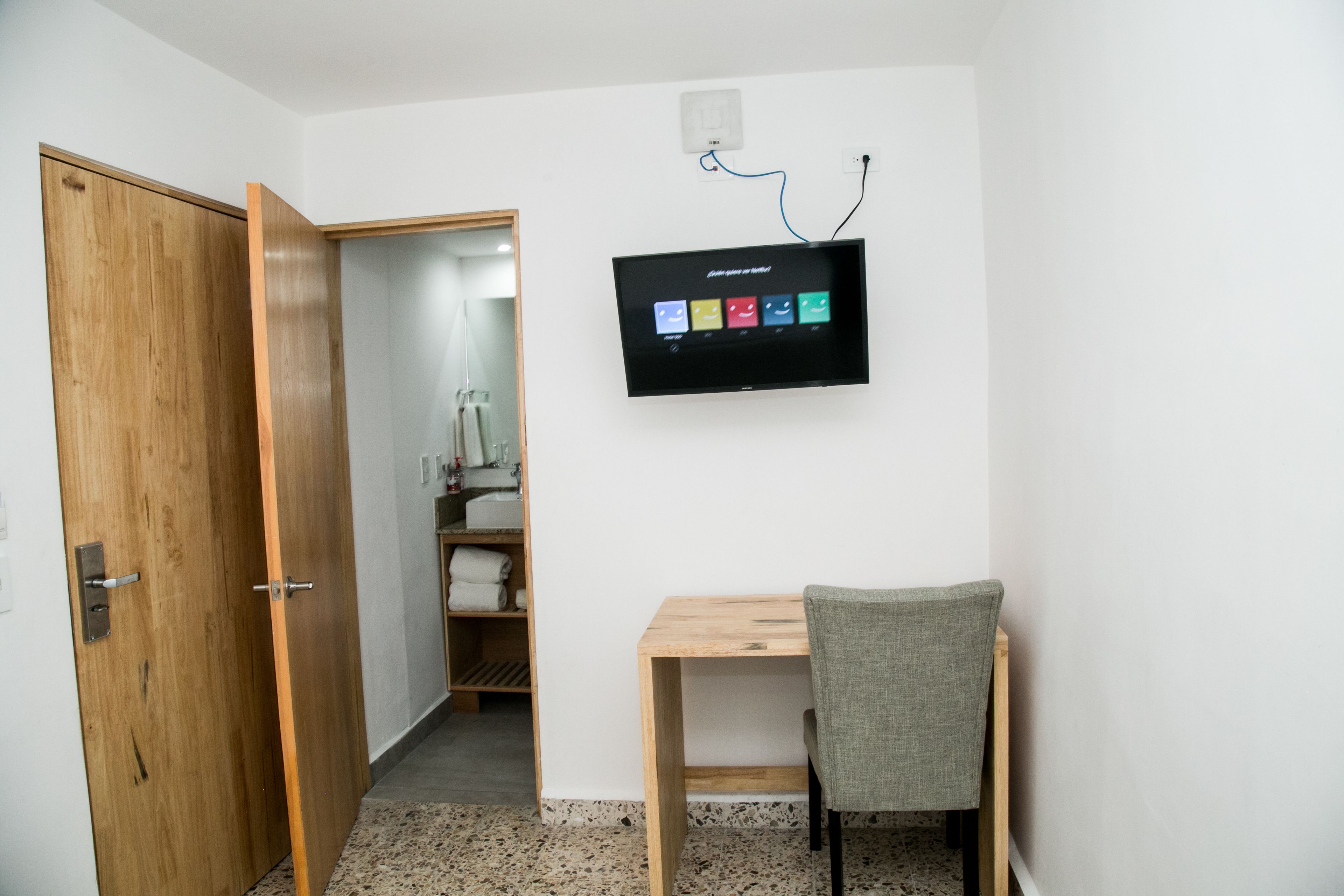Una habitación con un escritorio de madera, una silla, un televisor montado en la pared y un armario de madera.