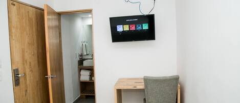 Una habitación con un escritorio de madera, una silla, un televisor montado en la pared y un armario de madera.