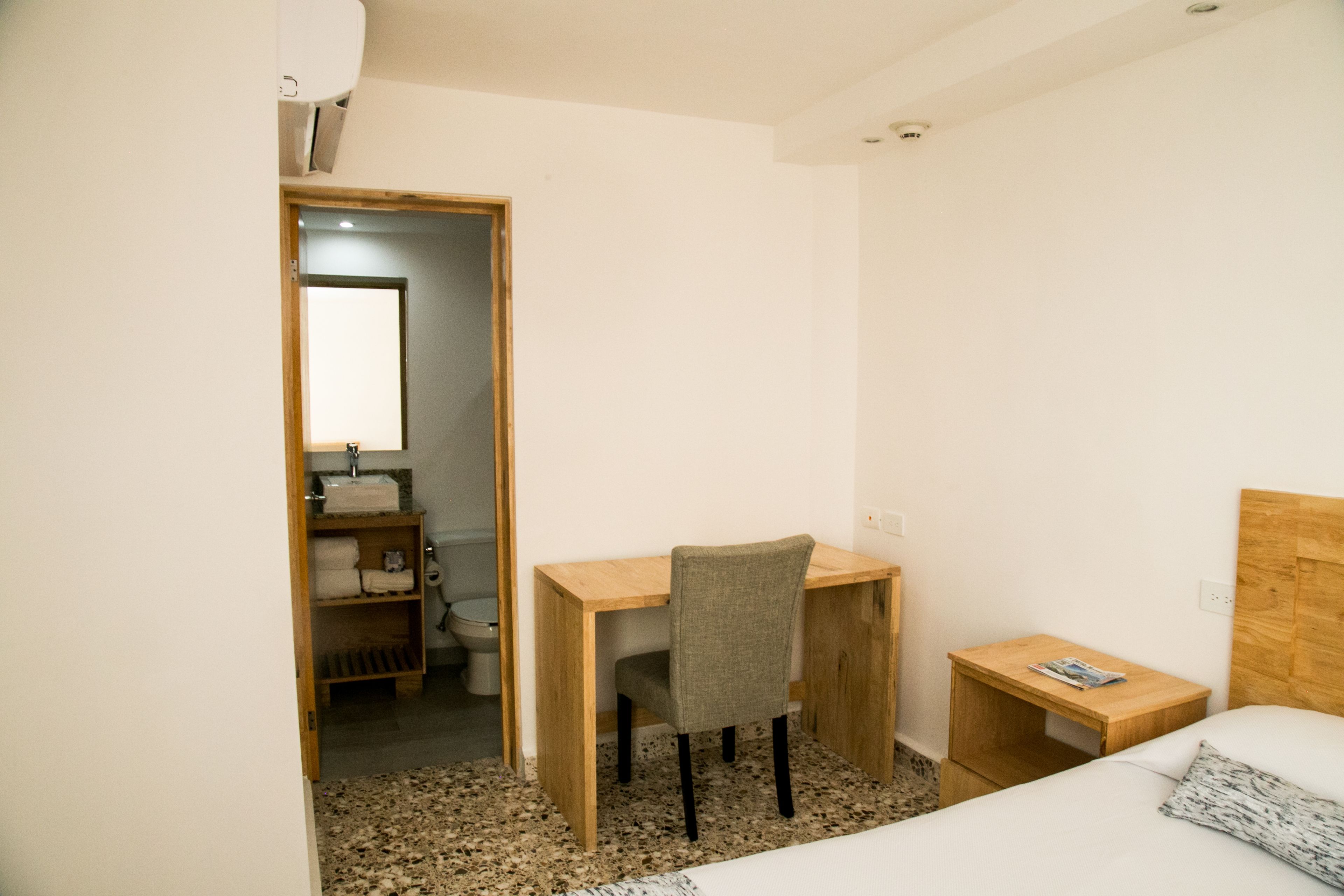 Una habitación pequeña y limpia con un escritorio de madera, una silla, una cama y una mesita de noche.