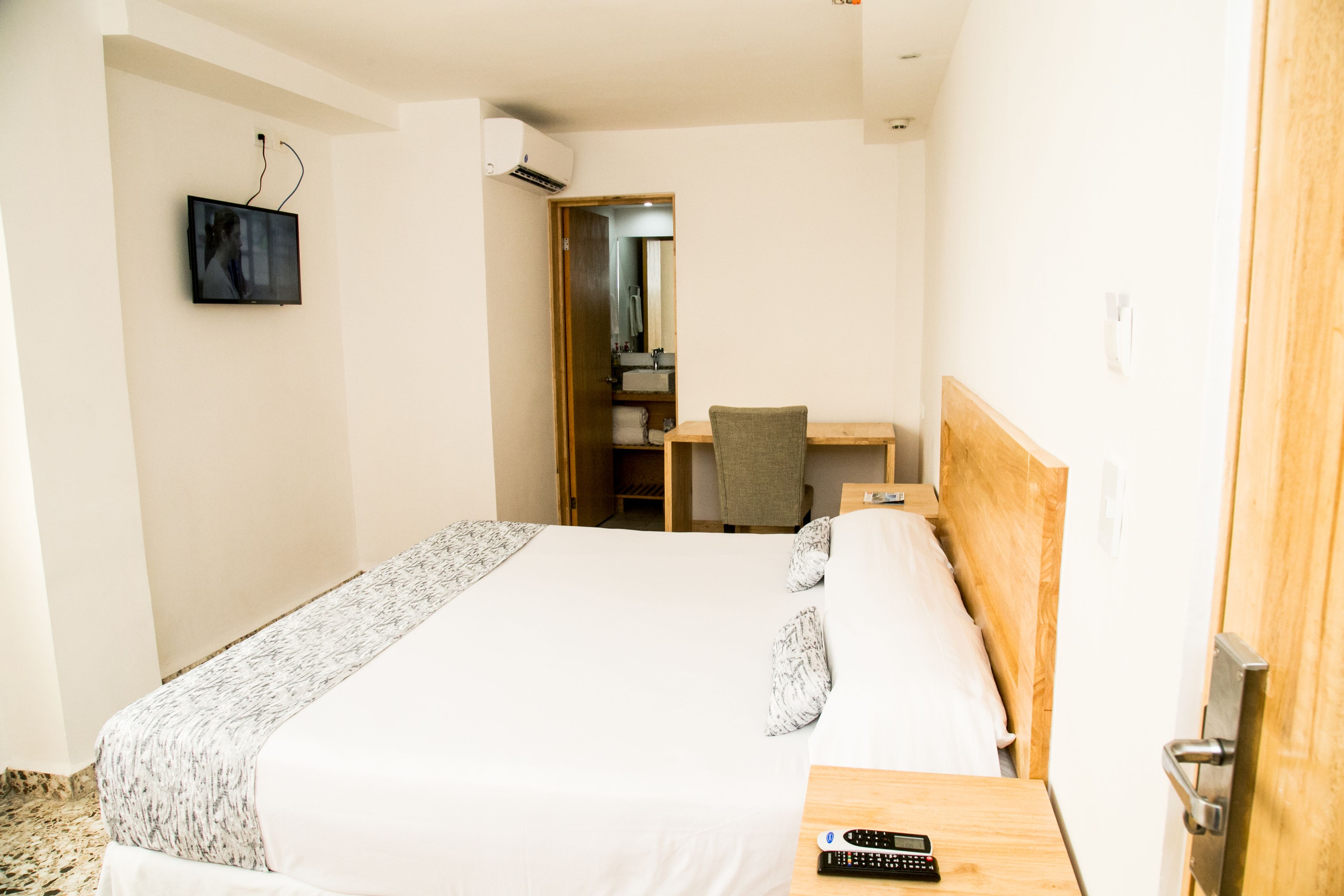 Una habitación de hotel con una cama, un escritorio, una silla, un televisor instalado en la pared y una puerta que da al baño.