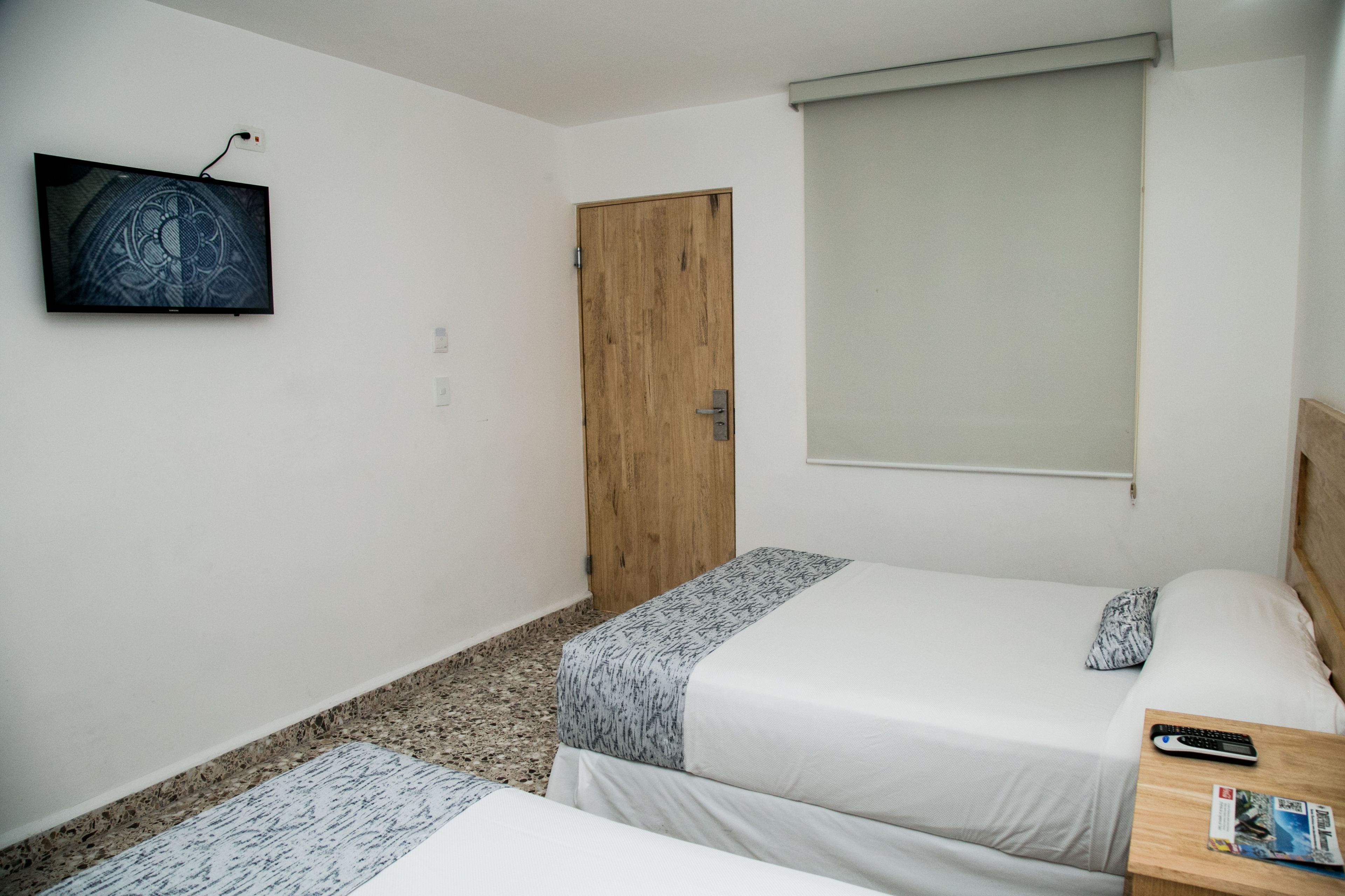 A small, clean room with two beds, a TV mounted on the wall, and a wooden door.