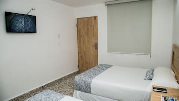 Ein kleiner, sauberer Raum mit zwei Betten, einem an der Wand befestigten Fernseher und einer Holztür.